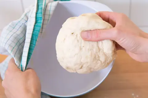 Hefeteig einfrieren: Eine Hand hält den Teig, die andere bedeckt eine Schüssel mit einem Küchentuch.