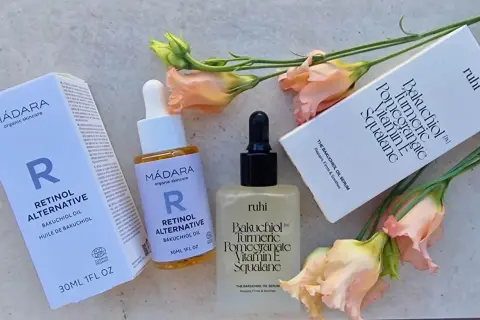 Zwei Hautpflegeprodukte mit Bakuchiol Öl, umgeben von zarten Blüten. Die Produkte versprechen eine sanfte Wirkung für straffere Haut.