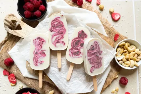 Eis am Stiel mit Himbeermuster, inspiriert von einfachen eis rezepte. Frische Himbeeren und Cashewkerne liegen daneben.