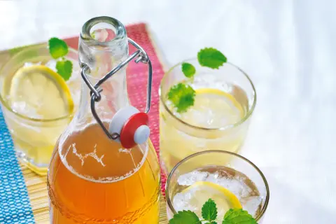 Erfrischender zitronenmelisse sirup in einer Bügelflasche, serviert mit Eis, Zitronenscheiben und Minze in Gläsern.