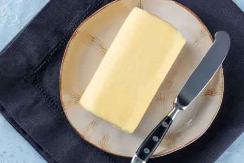 Ein Block Butter auf einem Teller mit einem Messer daneben. Die Frage, wie lange ist Butter haltbar, beschäftigt viele.