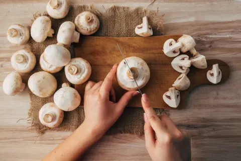 Hände schneiden frische Champignons für einen gesunden Snack. Roh essen ist eine tolle Option!