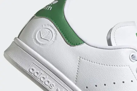 Detailaufnahme eines weißen Adidas Stan Smith Schuhs mit grünen Akzenten. Das vegane Siegel ist gut sichtbar. Perfekt für leichte, vegane Sommerschuhe.