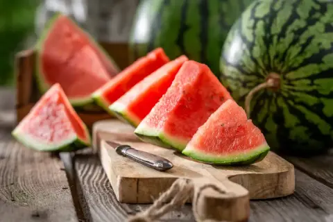 Saftige Wassermelonenstücke auf einem Holzbrett, daneben ganze Früchte. Die Wassermelone ist ein Sommergenuss, ihre Haltbarkeit ist bei richtiger Lagerung gut.