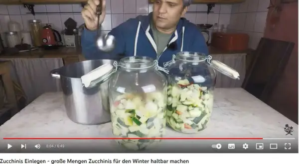 Mann füllt mit Schöpfkelle klein geschnittene Zucchini in Einmachgläser. Zucchini einwecken für den Winter.