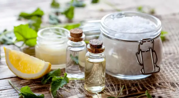 Zutaten für kosmetik selber machen: Zitrone, ätherische Öle, Salz und Kräuter auf Holzuntergrund.
