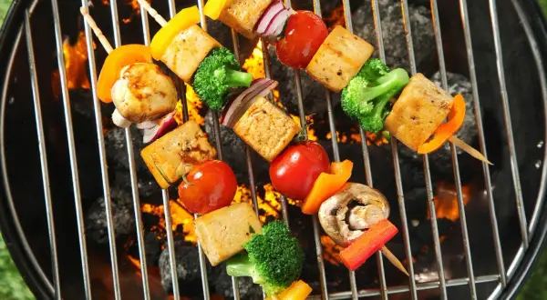 Vegane Grillrezepte: Bunte Gemüsespieße mit Tofu, Paprika, Brokkoli und Tomaten brutzeln auf dem Grill über glühender Kohle.