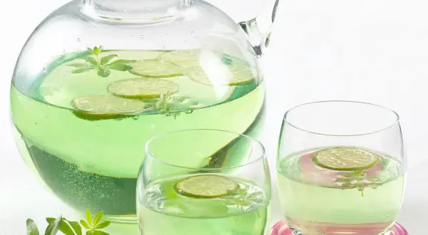 Erfrischendes Getränk mit Limettenscheiben und Waldmeister-Zweigen in einer Karaffe und Gläsern. Perfekt für Waldmeister Rezepte.