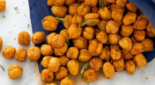 Knuspriger kichererbsen snack, gewürzt und mit Rosmarin verfeinert, liegt auf einem blauen Tuch und Marmor.