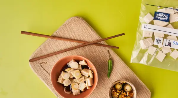Vorbereitung für tofu einfrieren: gewürfelter Tofu in Schüssel mit Soße, daneben ein kleiner Chili und ein Beutel mit gefrorenem Tofu.
