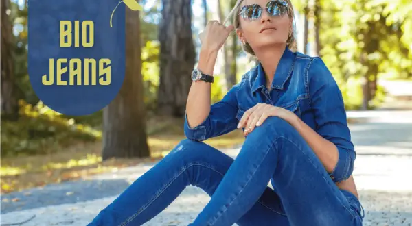 Frau in Jeansjacke und Hose, die entspannt im Park sitzt. "BIO JEANS" Schriftzug deutet auf nachhaltige deutsche Jeansmarken hin.