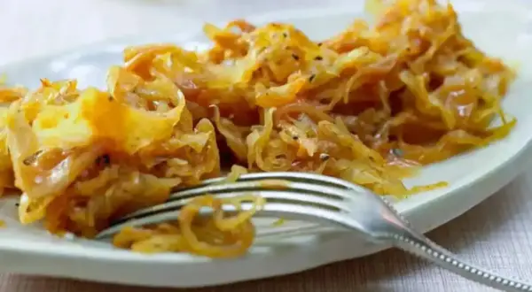 Ein Teller mit goldbraunem, gedünstetem Sauerkraut, das gerade mit einer Gabel serviert wird. Perfekt zum Sauerkraut kochen.