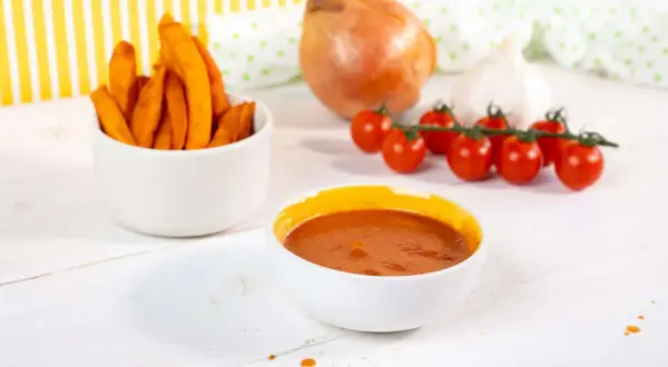 Süßkartoffel-Pommes mit selbstgemachtem Ketchup ohne Zucker. Zutaten wie Tomaten, Zwiebel und Knoblauch sind zu sehen.