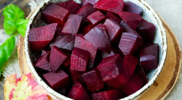 Schüssel mit gewürfelter roter Bete, die nach dem Kochen mit Essig glänzt. Ein Hauch von Herbst mit Blättern und Kräutern.