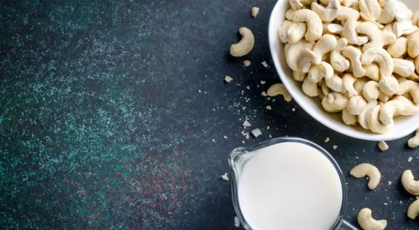 Cashewmilch selber machen ist einfach: Eine Schüssel voller Cashewkerne und ein Krug mit frischer Cashewmilch auf dunklem Untergrund.