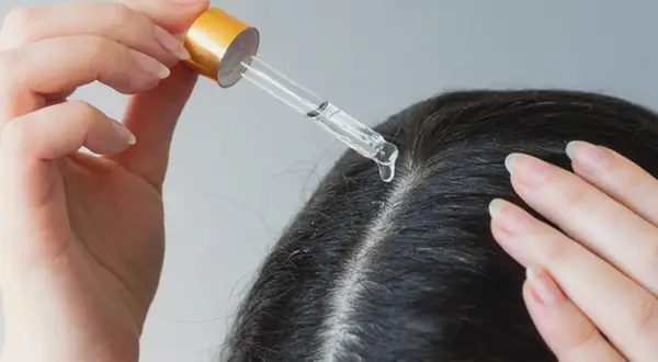 Eine Hand trägt mit einer Pipette ein Öl auf die Kopfhaut auf. Ein natürliches hausmittel gegen schuppen und juckende kopfhaut.