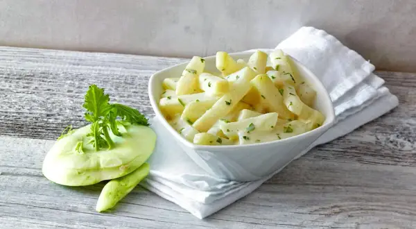 Schmackhafter Kohlrabi in cremiger Soße, daneben ein frischer Kohlrabi. Perfekt, wenn man wissen will, wie lange muss Kohlrabi kochen.