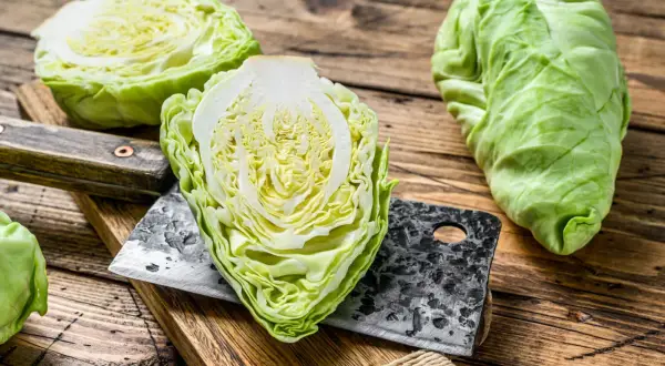 Frischer Spitzkohl, halbiert und auf einem Holzbrett mit einem Hackmesser. Perfekt, um Spitzkohl roh zu essen, als knackiger Salat.