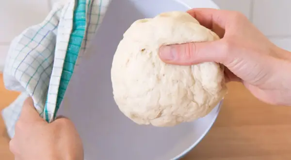 Hefeteig einfrieren: Eine Hand hält den Teig, die andere bedeckt eine Schüssel mit einem Küchentuch.