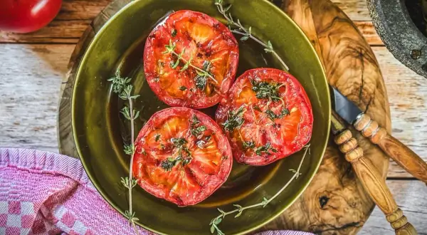 Drei saftige Scheiben Tomaten, perfekt gegrillt und mit frischen Kräutern bestreut, liegen auf einem grünen Teller. Ein Genuss für alle Sinne!