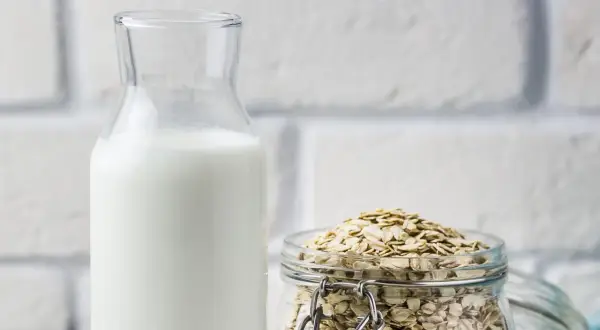 Glasflasche mit weißer Flüssigkeit neben einem Glas voller Haferflocken. Perfekt, um Hafermilch selber zu machen.