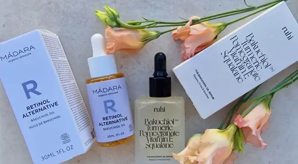 Zwei Hautpflegeprodukte mit Bakuchiol Öl, umgeben von zarten Blüten. Die Produkte versprechen eine sanfte Wirkung für straffere Haut.