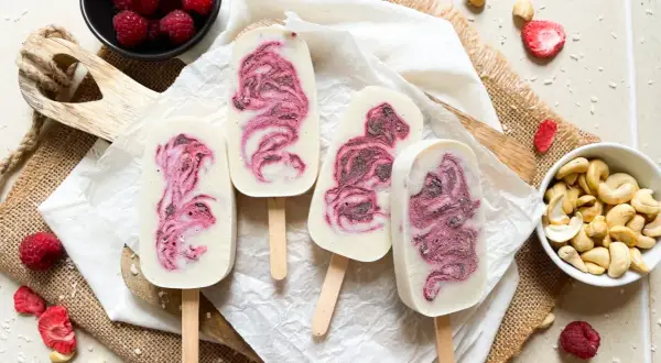 Eis am Stiel mit Himbeermuster, inspiriert von einfachen eis rezepte. Frische Himbeeren und Cashewkerne liegen daneben.