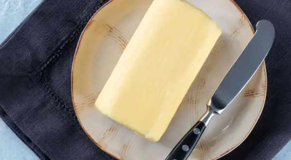 Ein Block Butter auf einem Teller mit einem Messer daneben. Die Frage, wie lange ist Butter haltbar, beschäftigt viele.