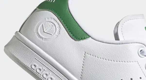 Detailaufnahme eines weißen Adidas Stan Smith Schuhs mit grünen Akzenten. Das vegane Siegel ist gut sichtbar. Perfekt für leichte, vegane Sommerschuhe.