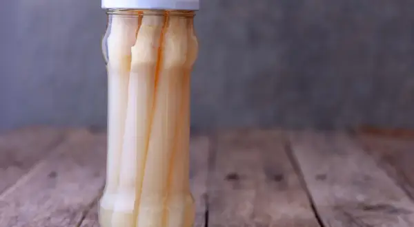 Ein Glas mit eingelegtem weißen Spargel steht auf einem Holztisch. Perfekt für das Spargel einkochen.