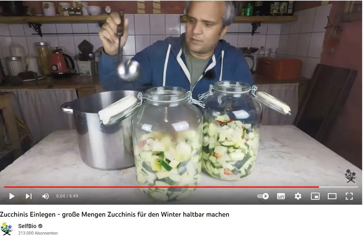 Mann füllt mit Schöpfkelle klein geschnittene Zucchini in Einmachgläser. Zucchini einwecken für den Winter.