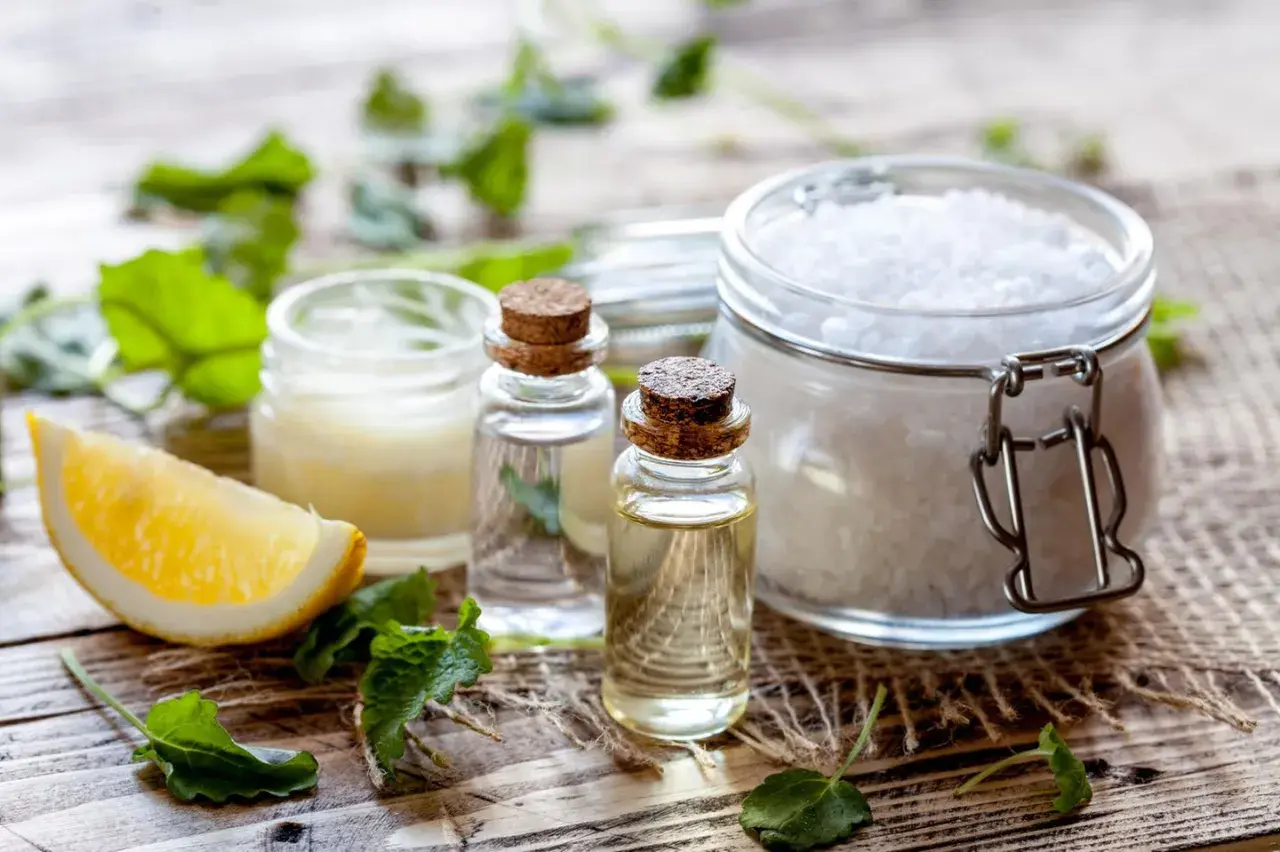 Zutaten für kosmetik selber machen: Zitrone, ätherische Öle, Salz und Kräuter auf Holzuntergrund.