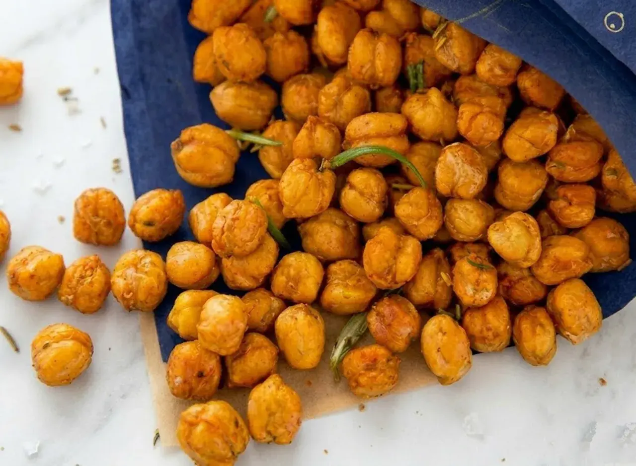 Knuspriger kichererbsen snack, gewürzt und mit Rosmarin verfeinert, liegt auf einem blauen Tuch und Marmor.