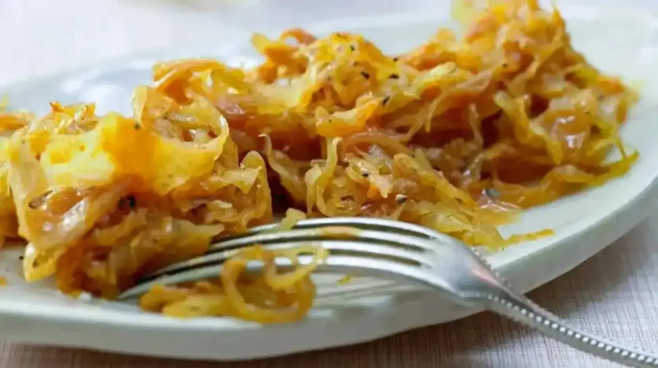 Ein Teller mit goldbraunem, gedünstetem Sauerkraut, das gerade mit einer Gabel serviert wird. Perfekt zum Sauerkraut kochen.