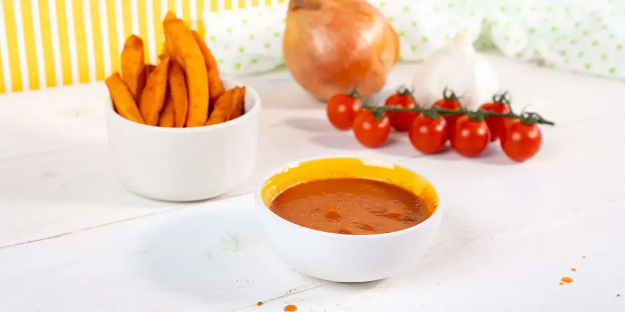 Süßkartoffel-Pommes mit selbstgemachtem Ketchup ohne Zucker. Zutaten wie Tomaten, Zwiebel und Knoblauch sind zu sehen.