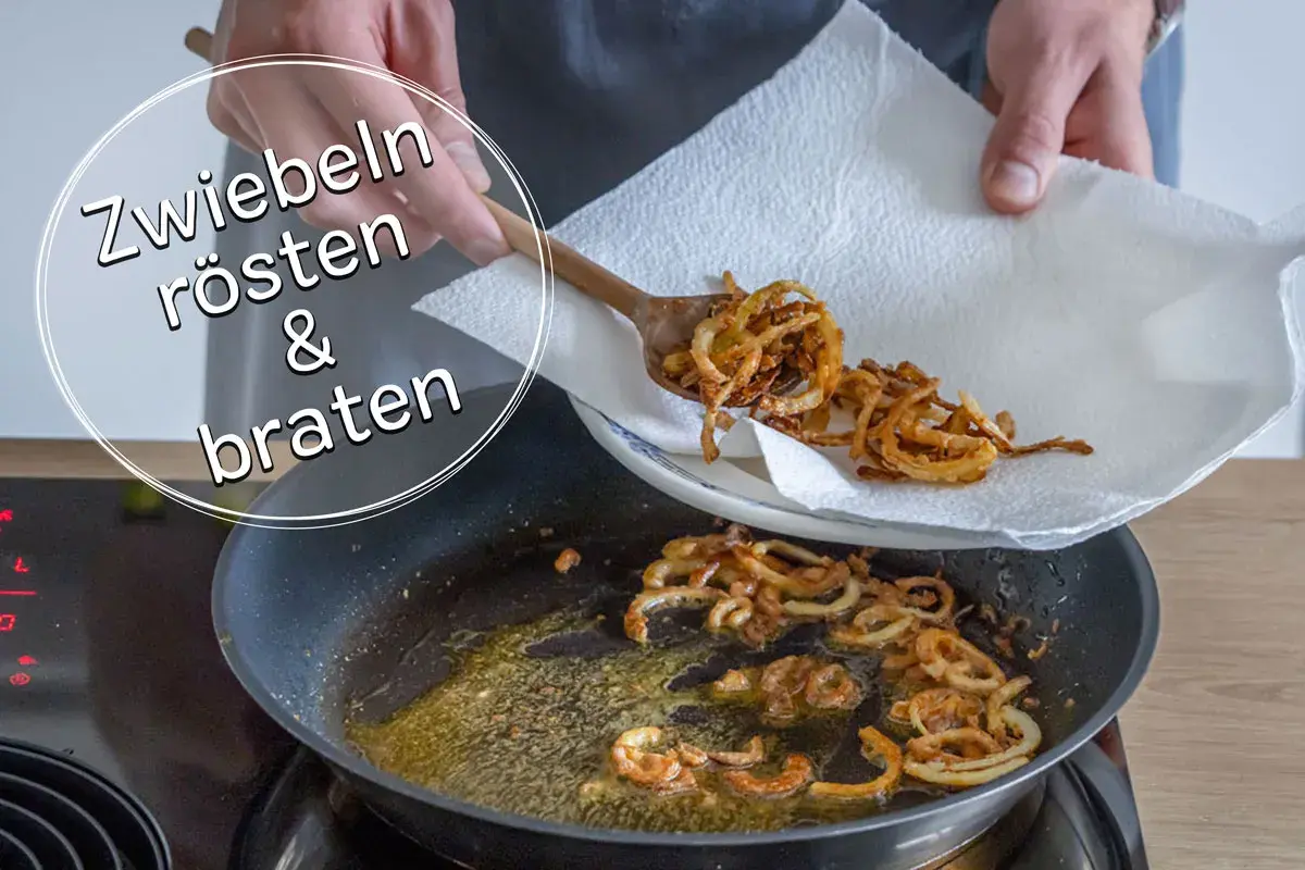Goldbraune, knusprige gebratene Zwiebeln werden mit einem Holzlöffel aus einer Pfanne auf Küchenpapier gehoben.