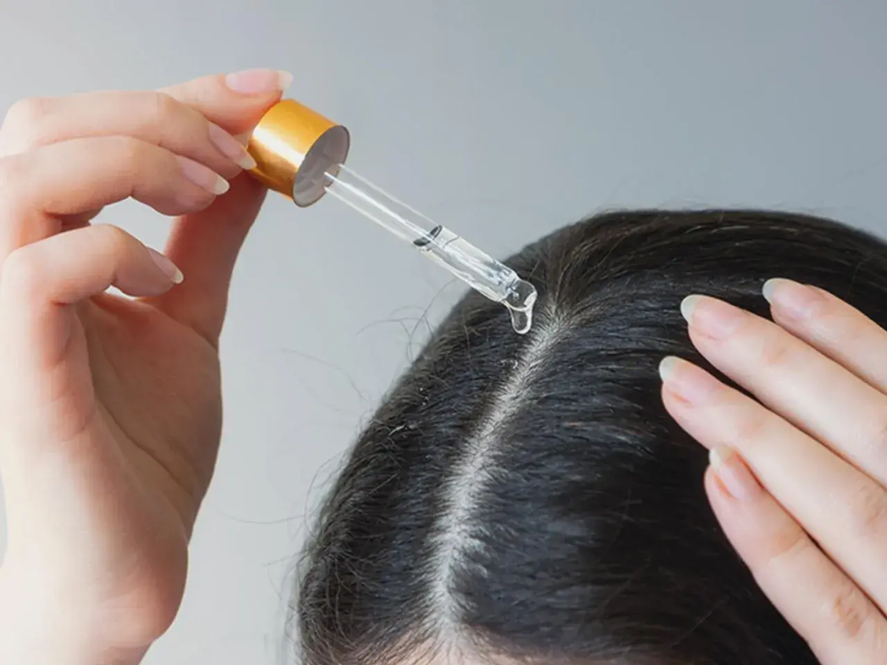 Eine Hand trägt mit einer Pipette ein Öl auf die Kopfhaut auf. Ein natürliches hausmittel gegen schuppen und juckende kopfhaut.