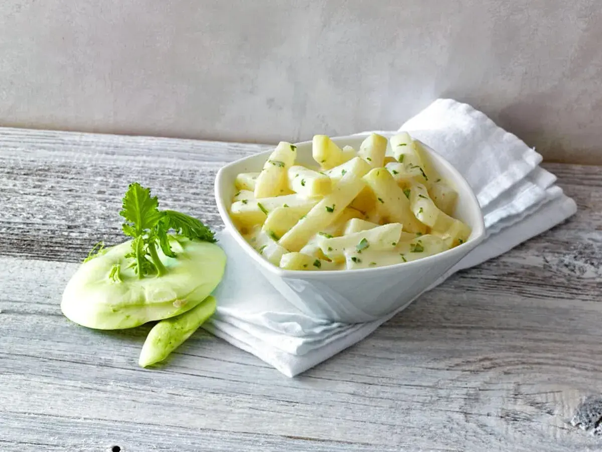 Schmackhafter Kohlrabi in cremiger Soße, daneben ein frischer Kohlrabi. Perfekt, wenn man wissen will, wie lange muss Kohlrabi kochen.