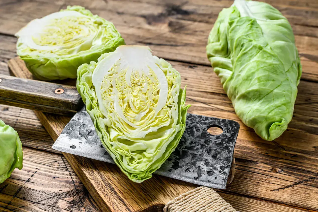 Frischer Spitzkohl, halbiert und auf einem Holzbrett mit einem Hackmesser. Perfekt, um Spitzkohl roh zu essen, als knackiger Salat.