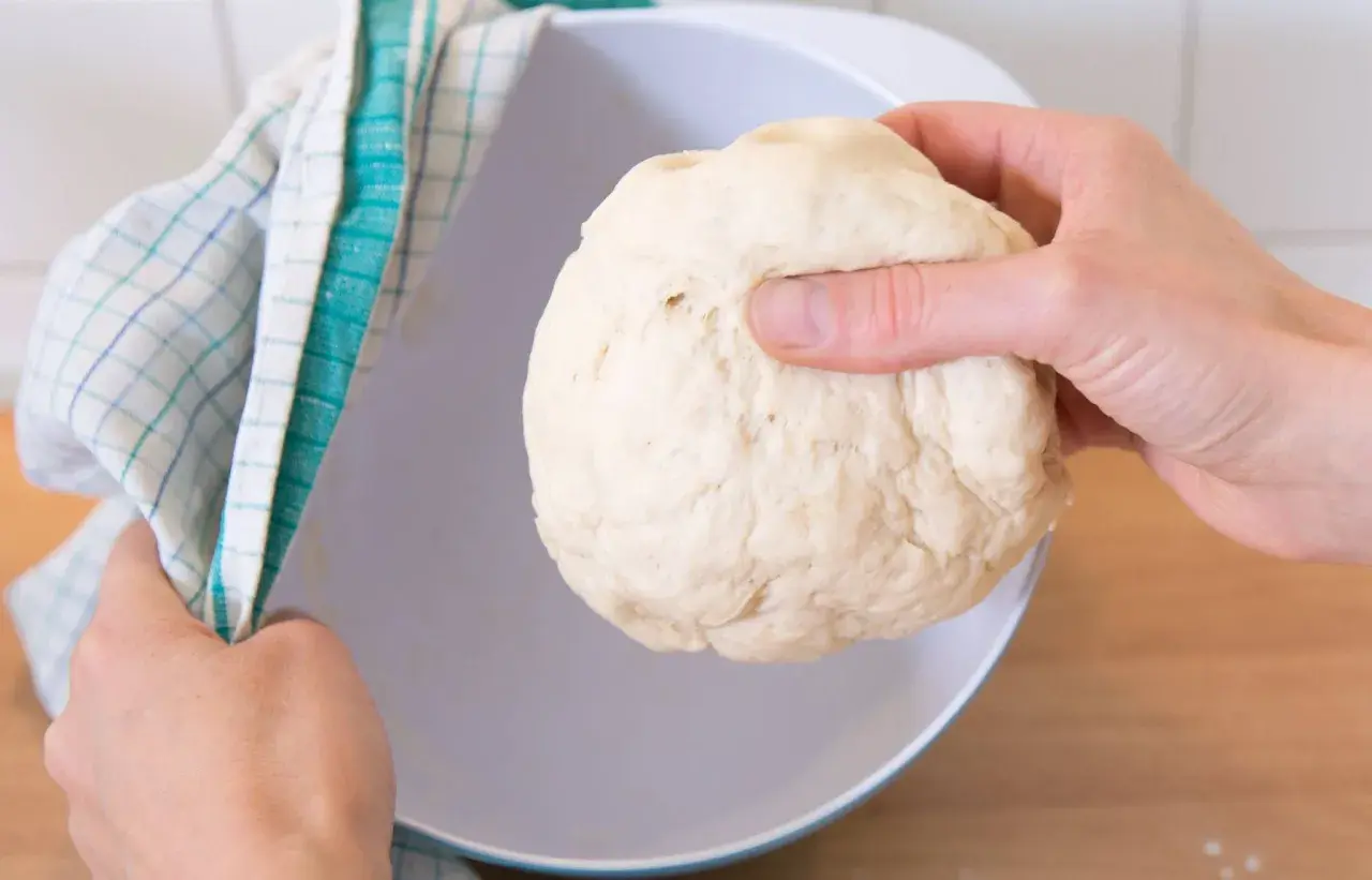 Hefeteig einfrieren: Eine Hand hält den Teig, die andere bedeckt eine Schüssel mit einem Küchentuch.