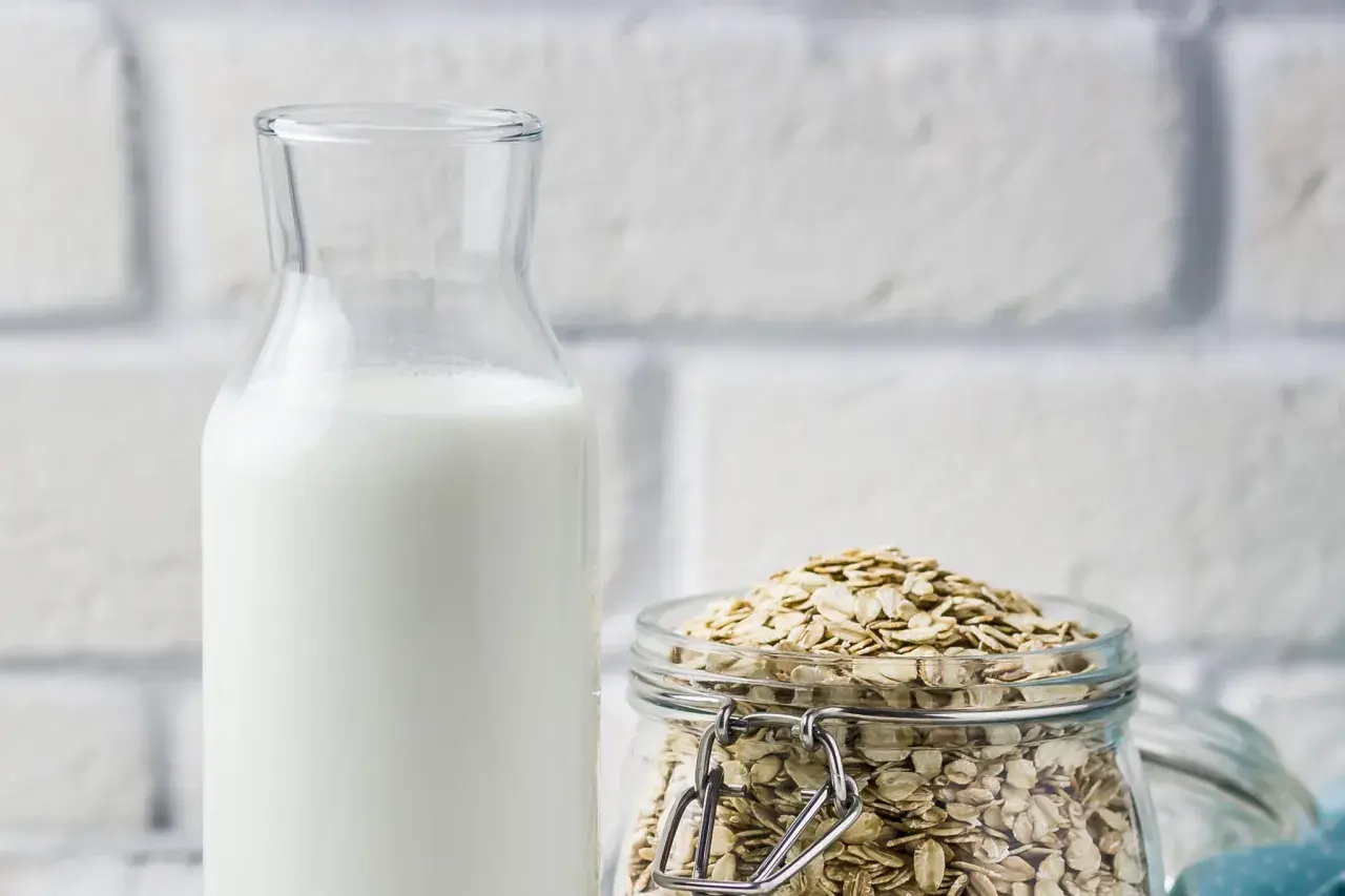 Glasflasche mit weißer Flüssigkeit neben einem Glas voller Haferflocken. Perfekt, um Hafermilch selber zu machen.