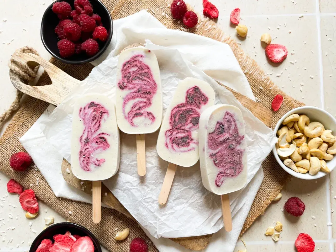 Eis am Stiel mit Himbeermuster, inspiriert von einfachen eis rezepte. Frische Himbeeren und Cashewkerne liegen daneben.
