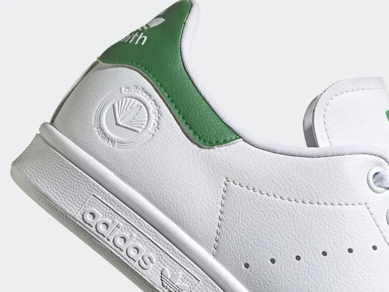 Detailaufnahme eines weißen Adidas Stan Smith Schuhs mit grünen Akzenten. Das vegane Siegel ist gut sichtbar. Perfekt für leichte, vegane Sommerschuhe.
