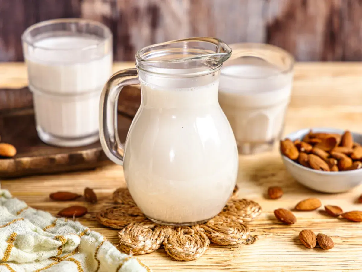 Frisch zubereitete Mandelmilch in einer Glaskaraffe, daneben Gläser und eine Schale mit Mandeln. So einfach ist Mandelmilch selber machen!
