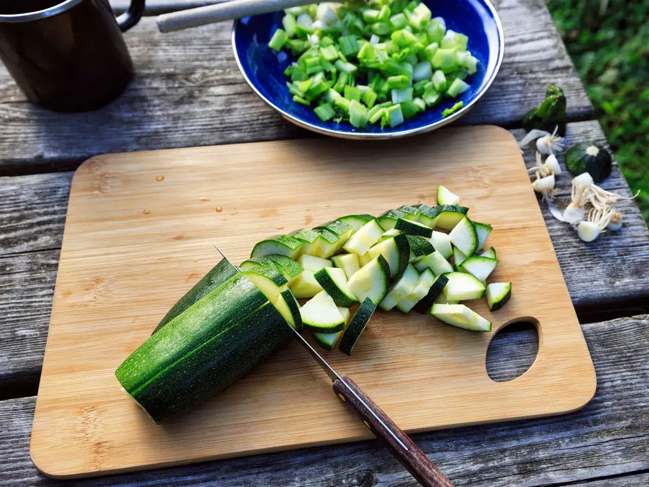 Zucchini wird in Scheiben geschnitten, bereit für das zucchini einfrieren. Daneben liegen kleine Zucchini und Knoblauch.