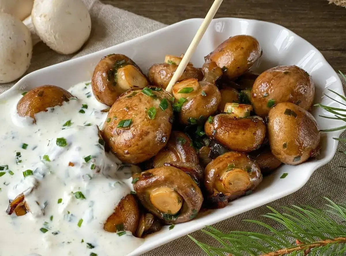 Leckere Champignons zubereiten: Gebratene Champignons mit Kräutercreme und Schnittlauch bestreut, serviert in einer weißen Schale.