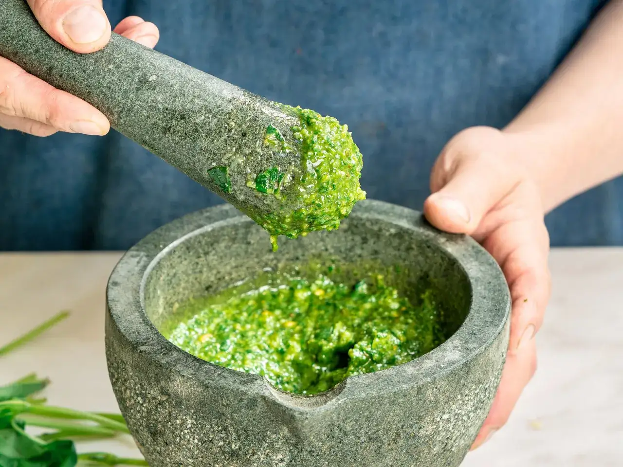 Frische Kr&auml;uter werden im M&ouml;rser zu selbstgemachtem Pesto zermahlen.
