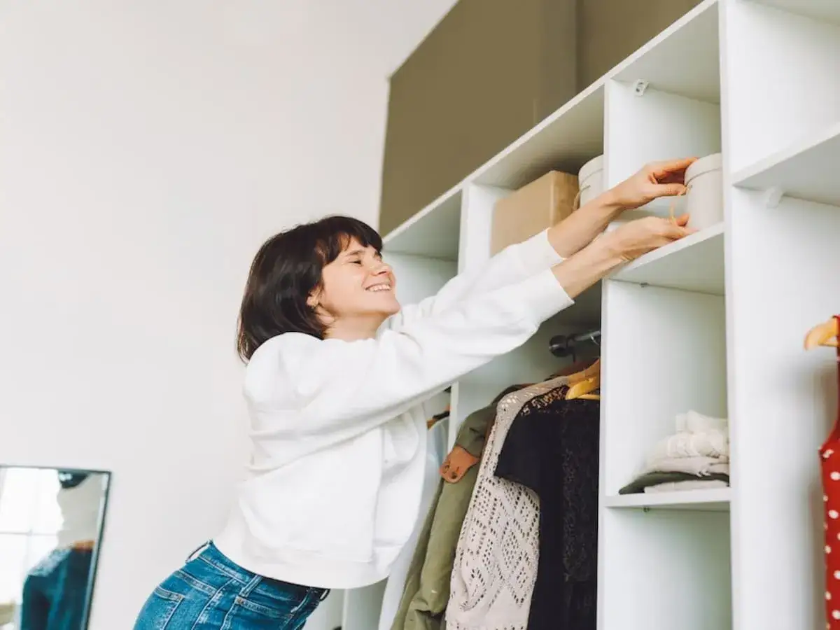 Frau räumt Kleiderschrank auf, der muffig riecht. Sie greift nach einer runden Box im obersten Fach.