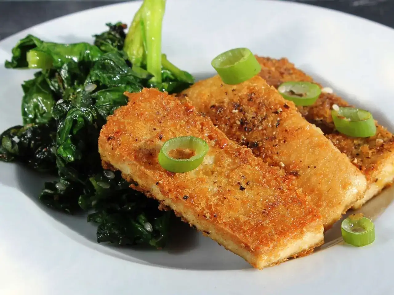 Knusprig paniertes Tofu auf einem Teller mit ged&uuml;nstetem gr&uuml;nen Gem&uuml;se, garniert mit Fr&uuml;hlingszwiebelringen. Perfekt f&uuml;r Tofu panieren.