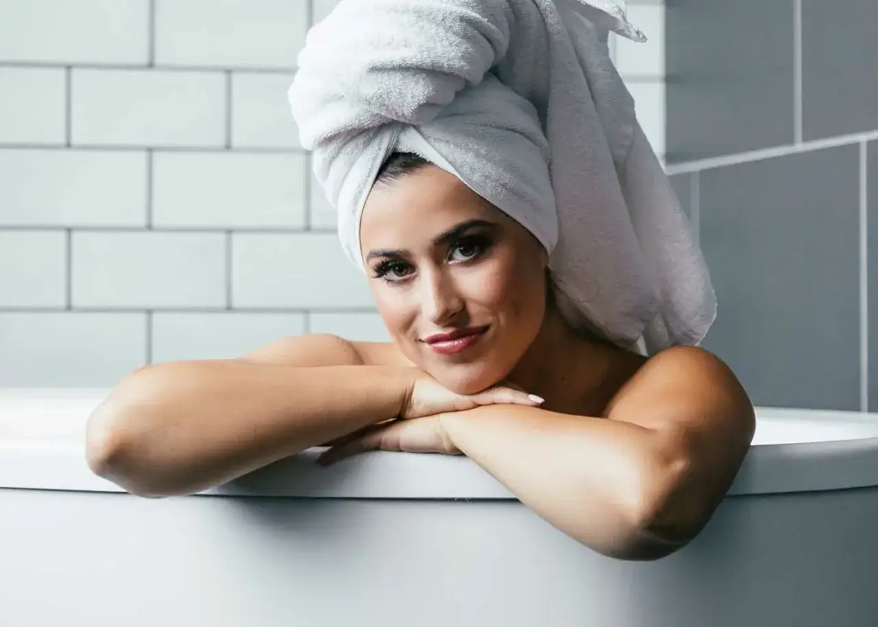 Frau mit Handtuch auf dem Kopf entspannt in der Badewanne. Die Wirkung eines Natronbades kann Wunder wirken für Haut und Wohlbefinden.